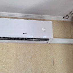 INSTALSERW - ROMAN RACZEK - Biała jednostka klimatyzatora ściennego KAISAI z wyświetlaczem '22', zamontowana na beżowej ścianie z marmurkowym wzorem, z maskownicą instalacji i rurkami biegnącymi do sufitu.