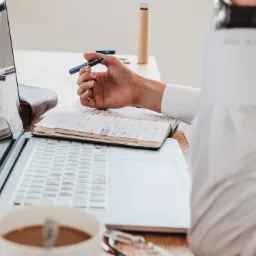 Tłumacz trzymający pióro nad otwartym paszportem obok laptopa i filiżanki kawy, przygotowując się do tłumaczenia dokumentów.
