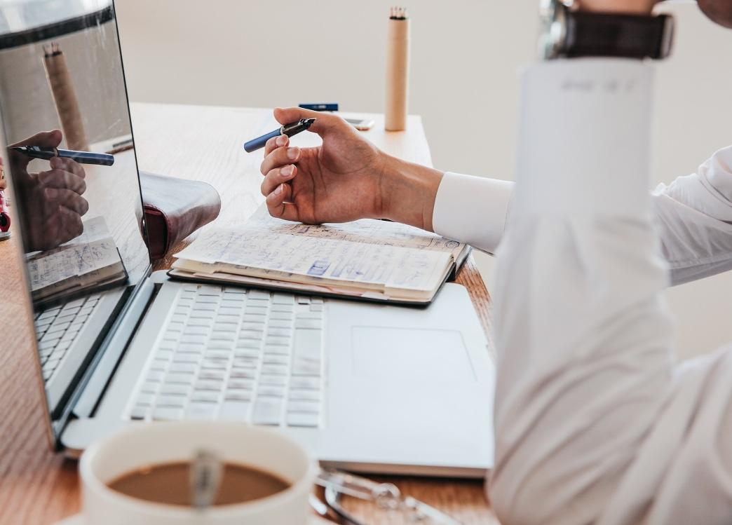 Tłumacz trzymający pióro nad otwartym paszportem obok laptopa i filiżanki kawy, przygotowując się do tłumaczenia dokumentów.