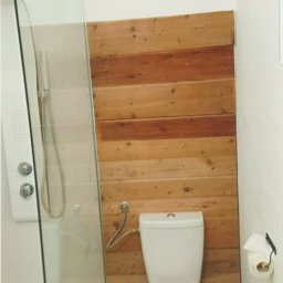 Maciej Rosiński - Nowoczesna łazienka z kabiną prysznicową i toaletą na tle ściany z drewnianych paneli, widoczny również uchwyt na papier toaletowy.