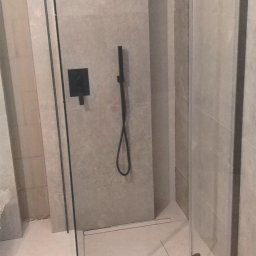 Maciej Rosiński - Kabina prysznicowa typu walk-in z czarnymi elementami armatury, zamontowana na jasnych płytkach w minimalistycznej łazience.