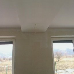 Maciej Rosiński - Ściana i sufit w trakcie prac przygotowawczych, widoczne ślady po szpachlowaniu, wystający kabel elektryczny, okna z widokiem na krajobraz za oknem.