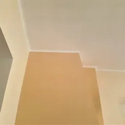 Świeżo odmalowany narożnik pomieszczenia w Katowicach, gdzie ściana w odcieniu beżu łączy się z białym sufitem, widoczne precyzyjne odcięcie kolorów.
