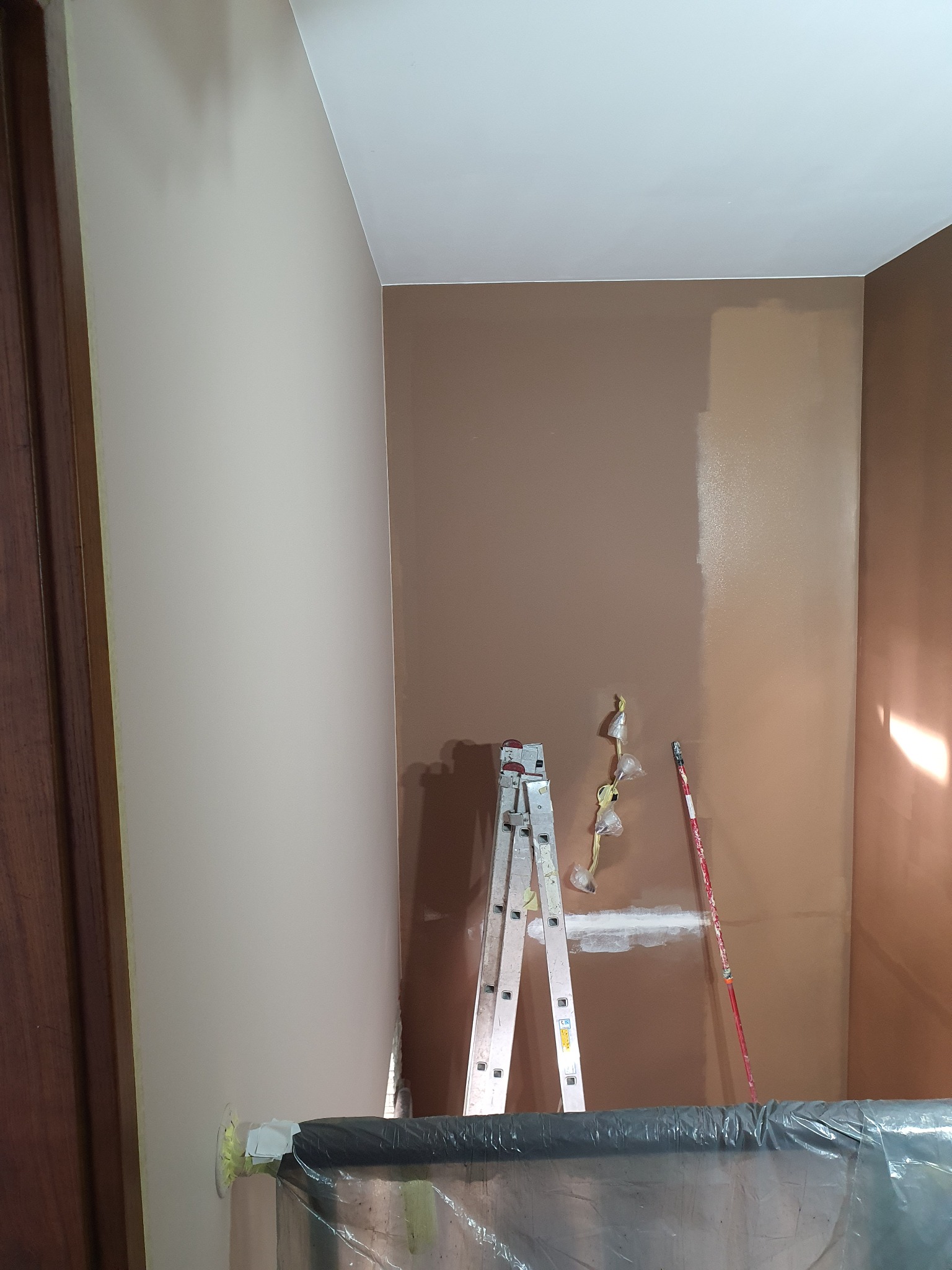 Malowanie ścian na brązowo w trakcie remontu; widoczna drabina, wałek do malowania, zabezpieczone gniazdka i folia ochronna na podłodze.