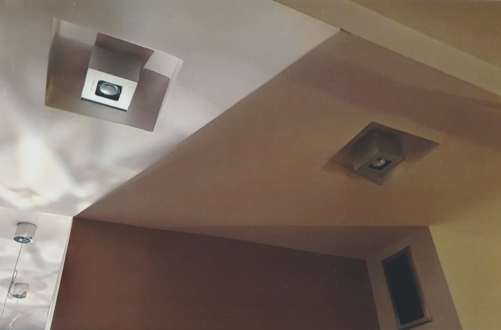 Kąt sufitu po odświeżeniu, z dwoma kwadratowymi lampami wpuszczonymi w sufit, ściany w odcieniach brązu i beżu.