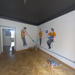 DANIEL DOMAŃSKI - Wnętrze pokoju z pomalowanym na czarno sufitem i białymi ścianami, na których widnieją barwne, stylizowane postacie dmuchaczy szkła, na podłodze parkiet ułożony w jodełkę, widoczna drabina malarska...