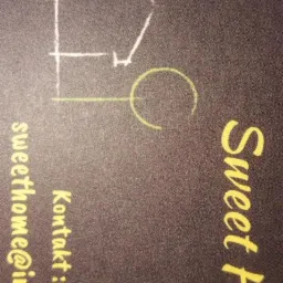 Wizytówka firmy 'Sweet Home' z Łomży, prezentująca schematyczny rysunek domu w białym kolorze i dane kontaktowe w żółtym, na ciemnym tle.