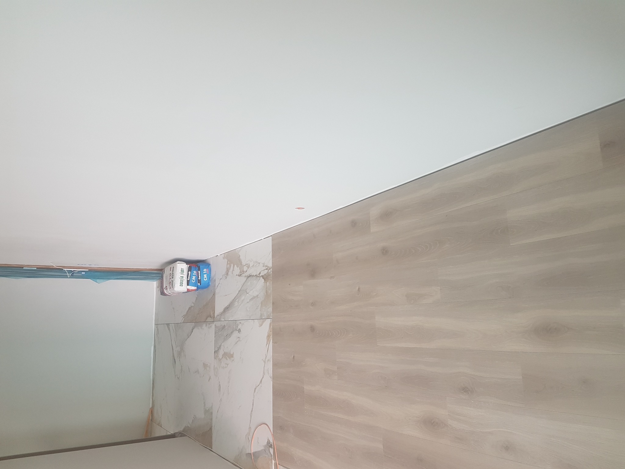 Łazienka po remoncie: połączenie płytek imitujących marmur i paneli podłogowych, widoczne worki z klejem do płytek Cersanit.