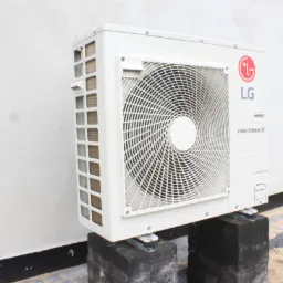 Zewnętrzna jednostka klimatyzacji LG Therma V, zamontowana na betonowych podstawach przy ścianie budynku, widoczna z boku z lekkim kątem.