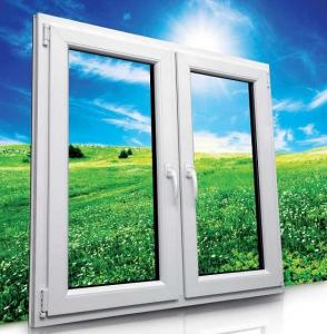 Białe okno PCV z podwójnymi szybami, widok na zielone pole i błękitne niebo z chmurami, odbicie w dolnej części ramy.