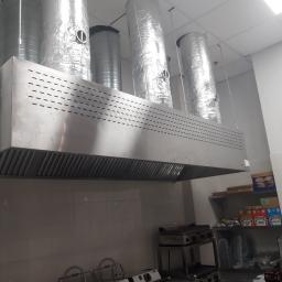 Bakbud Sp. z o.o. - Profesjonalny system wentylacyjny ze stali nierdzewnej w kuchni komercyjnej, z widocznymi kanałami wentylacyjnymi owiniętymi folią aluminiową, zainstalowany nad sprzętem kuchennym.