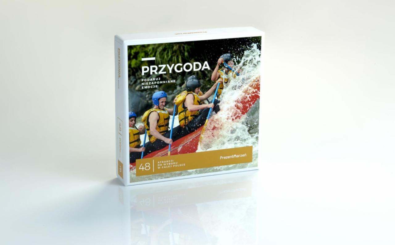 Pudełko prezentowe z grafiką raftingu na wzburzonej wodzie, z napisem 'Przygoda' i 'Podaruj niezapomniane emocje', odbicie pudełka na błyszczącej powierzchni.