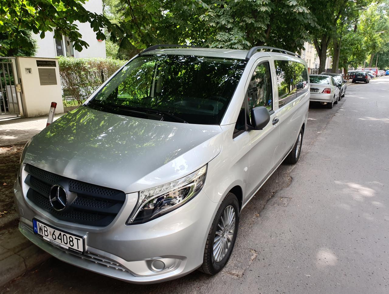 Srebrny Mercedes Vito zaparkowany na ulicy, widoczne drzewa i budynek w tle, tablica rejestracyjna WB 6408T.