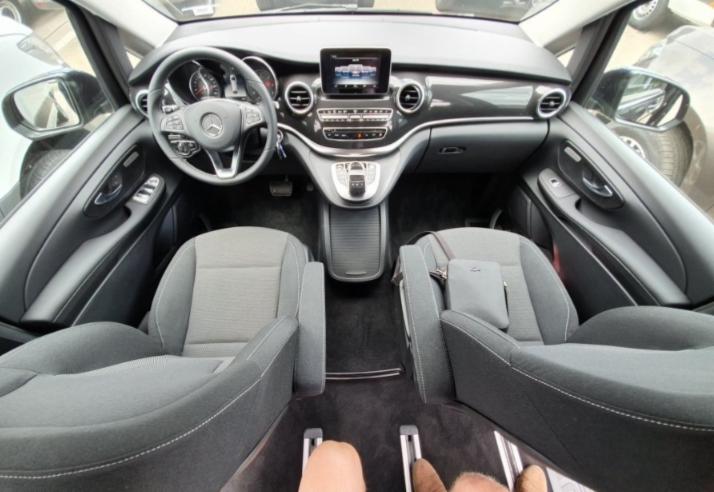 Wnętrze przestronnego samochodu osobowego marki Mercedes z jasnoszarymi fotelami i czarną deską rozdzielczą, widok z perspektywy pasażera z tyłu.