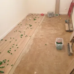 Układanie drewnopodobnych płytek podłogowych z użyciem zielonych klinów poziomujących w trakcie remontu pomieszczenia.