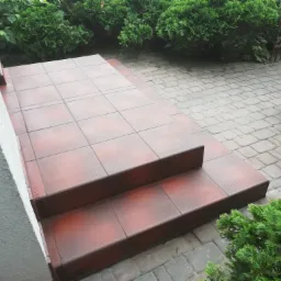 Wykończone płytkami ceramicznymi schody wejściowe do domu, widok z góry, zieleń w tle.