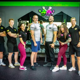 Fit & Fizjo Team - trening personalny, fizjoterapia, masaże Gdańsk - Grupa sześciu osób, w tym dwie kobiety, w strojach sportowych, pozujących w siłowni przed lustrem z widocznym logo Fit&Fiz Studio, obok sprzęt do ćwiczeń.