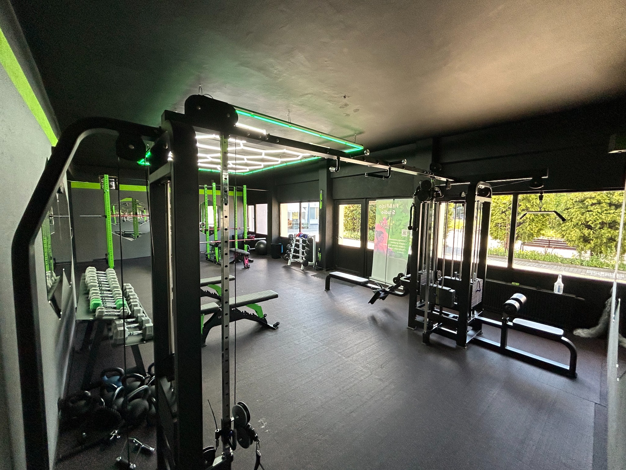 Nowoczesna siłownia z czarnymi ścianami i zielonymi akcentami, widok na różnorodne maszyny do ćwiczeń i hantle