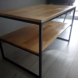 Stolik kawowy z blatem z jasnego drewna i czarną, metalową konstrukcją, widoczny na tle podłogi z paneli.