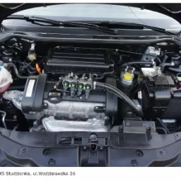 Silnik samochodu z zamontowaną instalacją LPG, widoczne wtryskiwacze gazu z zielonymi końcówkami, zbiornik płynu chłodniczego z niebieską nakrętką, czarny akumulator, otwarty przedni panel...