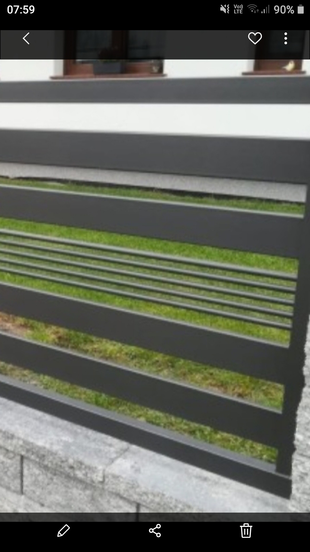 Nowoczesne, poziome przęsło ogrodzeniowe w kolorze grafitowym, zamontowane na murku z szarej kostki, z widokiem na trawnik w tle.