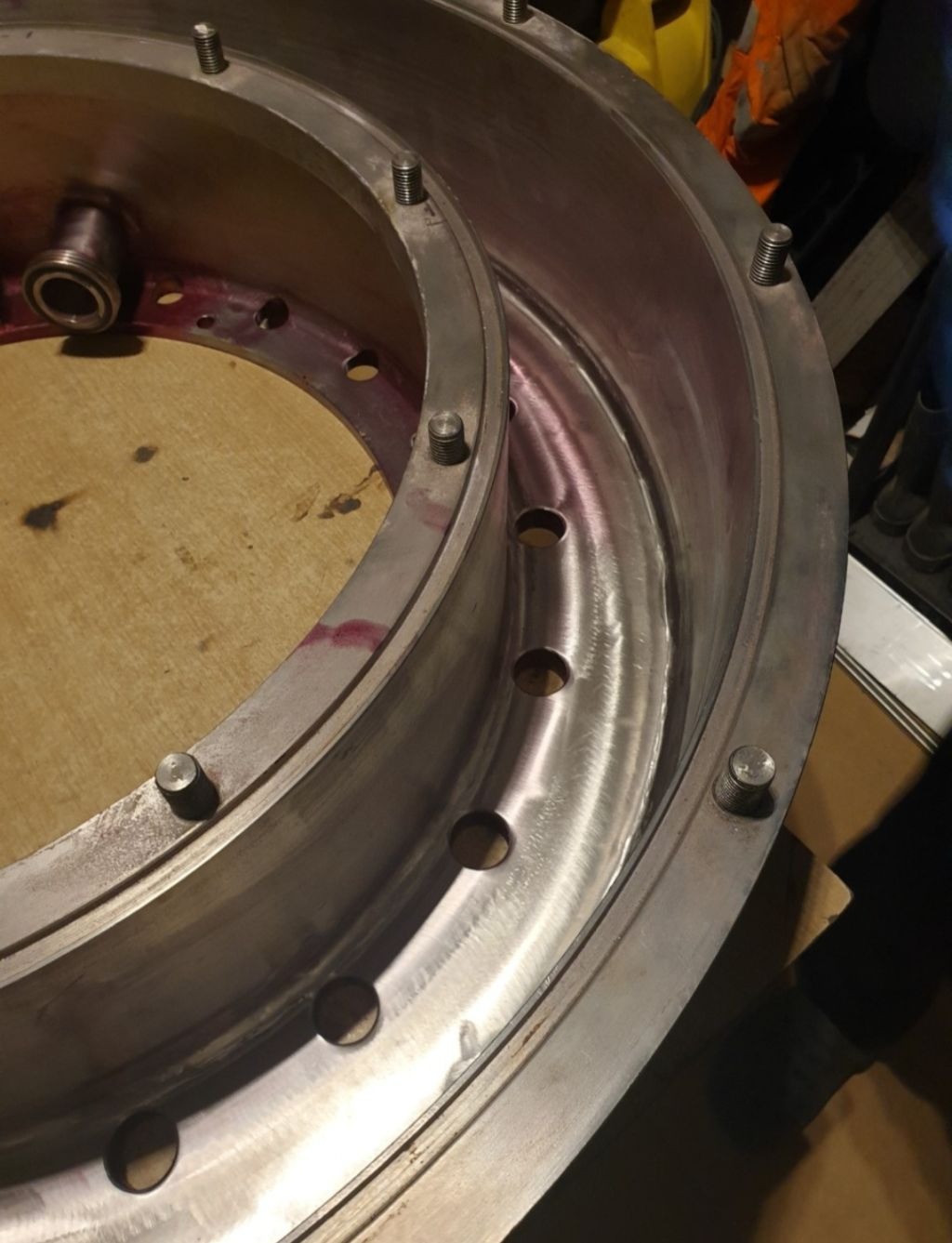 Metalowa konstrukcja pierścieniowa z widocznymi śladami czerwonego barwnika penetracyjnego, mocowana śrubami, prawdopodobnie w trakcie kontroli jakości spoin.