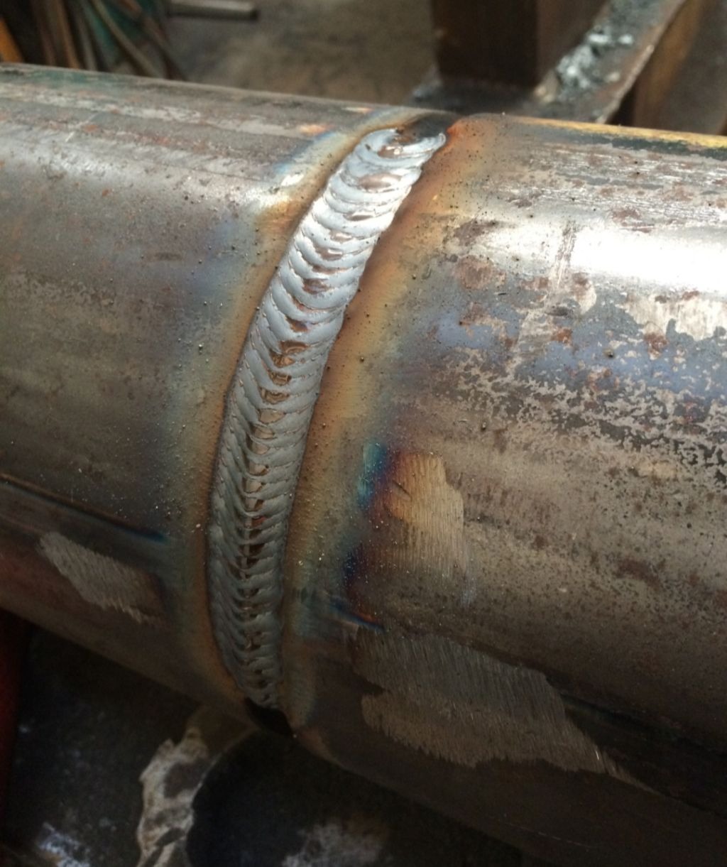 Szczegółowe zbliżenie spoiny na okrągłym elemencie metalowym, widoczne ślady obróbki i przebarwienia termiczne.