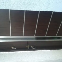 Ciemnobrązowe drzwi wejściowe z poziomym przeszkleniem i srebrnymi paskami dekoracyjnymi, widoczne dwa zamki z kluczami, zamontowane w ościeżnicy z widoczną pianką montażową.