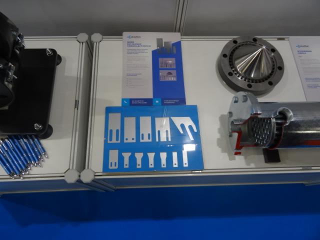 Ekspozycja z elementami maszyn: przekrój wymiennika ciepła, kołnierz z dyszą stożkową, niebieska plansza z wyciętymi kształtami metalowymi.