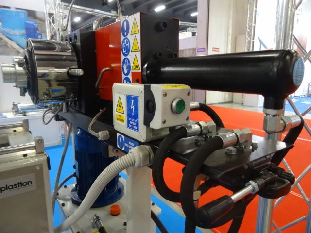 Detale przemysłowej maszyny z elementami hydraulicznymi, widoczne tabliczki ostrzegawcze i przycisk sterujący.