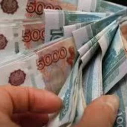 Dłonie trzymające plik banknotów rosyjskich rubli o nominale 5000 i 50 rubli, widoczna część klawiatury w tle.