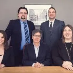 Grupa pięciu profesjonalnie ubranych os&oacute;b (trzech mężczyzn i dwie kobiety) pozuje za biurkiem, z obrazem w ramie na ścianie w tle.