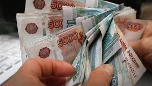 Dłonie trzymające plik banknotów rosyjskich rubli o nominale 5000 i 50 rubli, widoczna część klawiatury w tle.