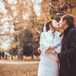 Veludo - Pocałunek nowożeńców w jesiennej scenerii parku w Warszawie, panna młoda w białej sukni z bolerkiem i koronkowymi rękawiczkami, pan młody w ciemnym płaszczu.