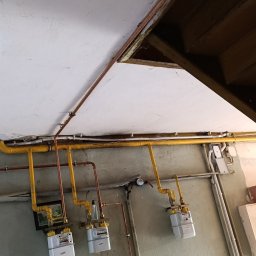 PHU KRISMART - Trzy nowe gazomierze zamontowane na ścianie w pomieszczeniu z widocznymi rurami miedzianymi i żółtymi instalacjami gazowymi pod sufitem z widocznymi elementami konstrukcyjnymi dachu.