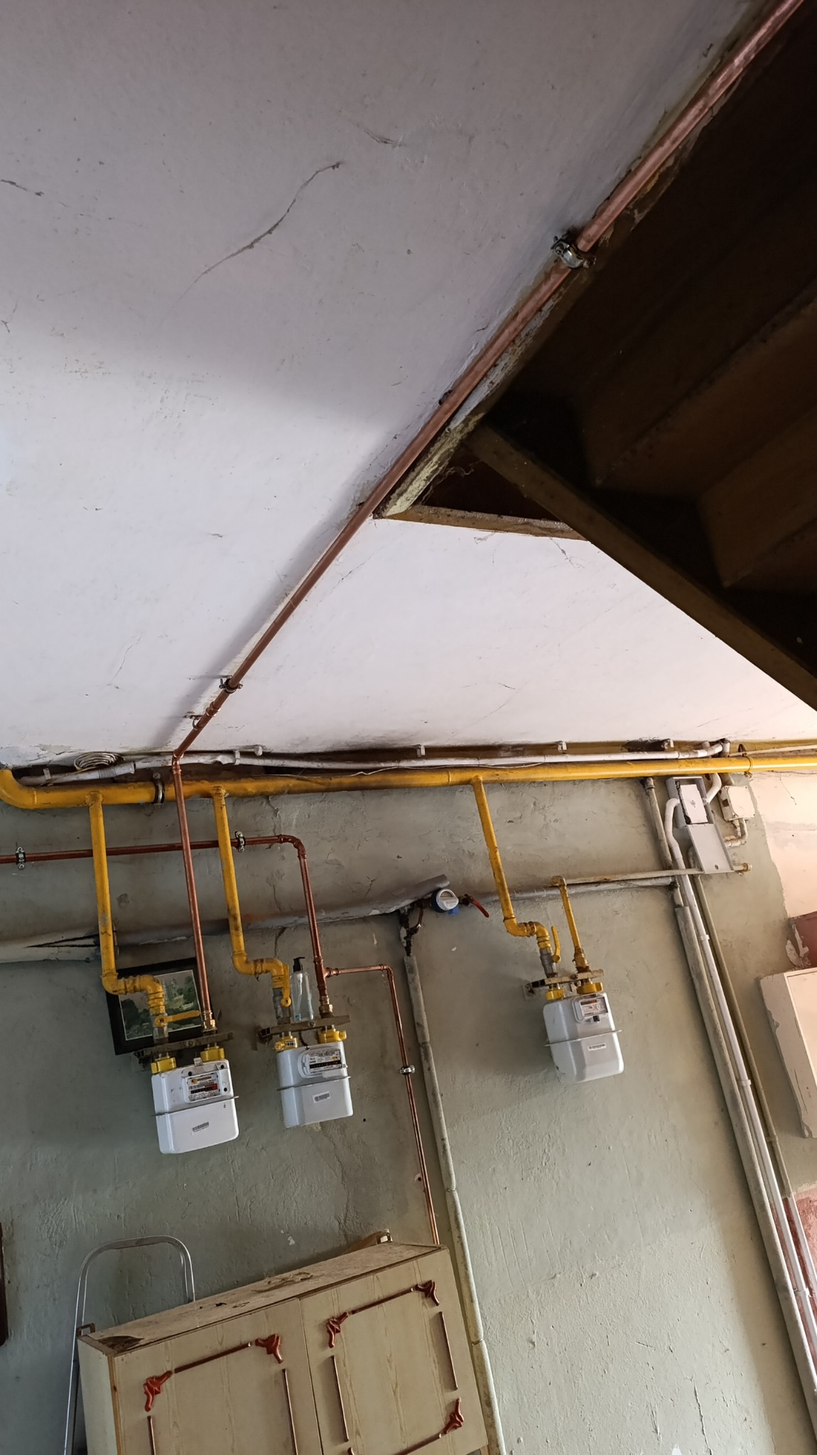 Trzy nowe gazomierze zamontowane na ścianie w pomieszczeniu z widocznymi rurami miedzianymi i żółtymi instalacjami gazowymi pod sufitem z widocznymi elementami konstrukcyjnymi dachu.