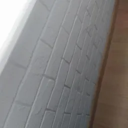 Ściana pokryta szarą farbą imitującą cegłę, widoczny fragment drewnianej podłogi.