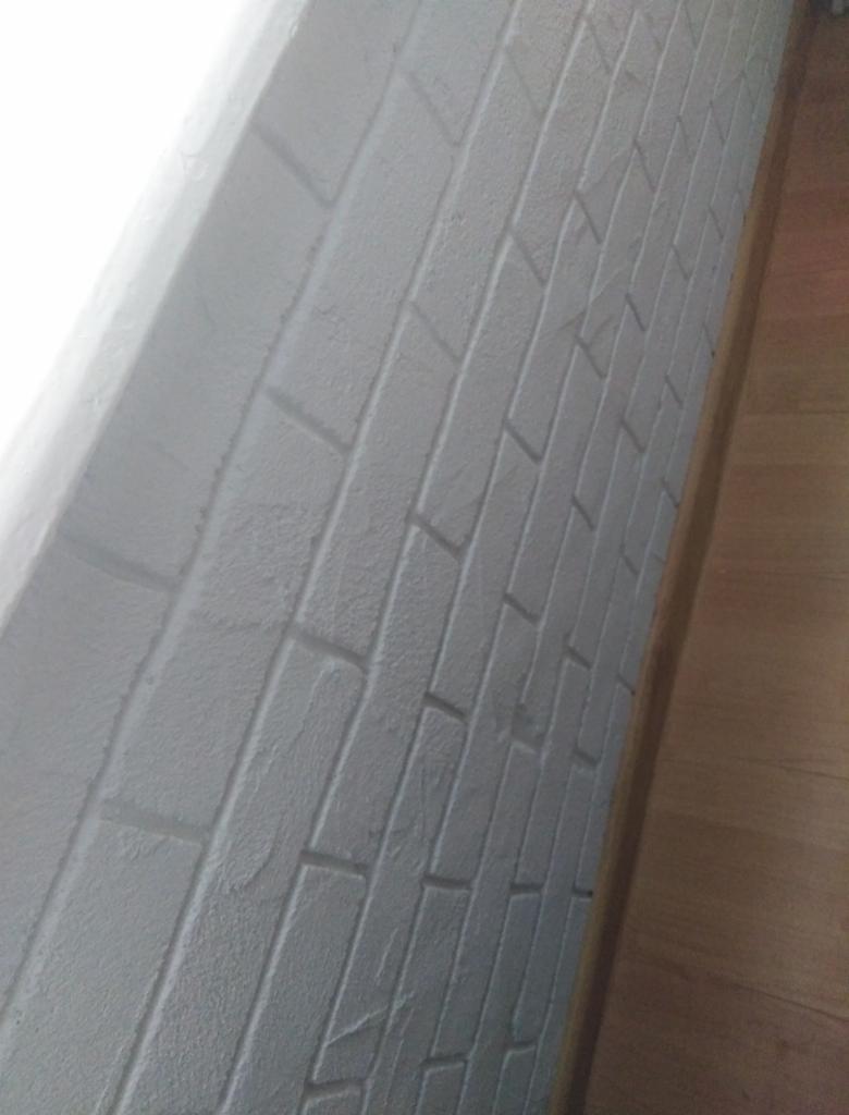 Ściana pokryta szarą farbą imitującą cegłę, widoczny fragment drewnianej podłogi.