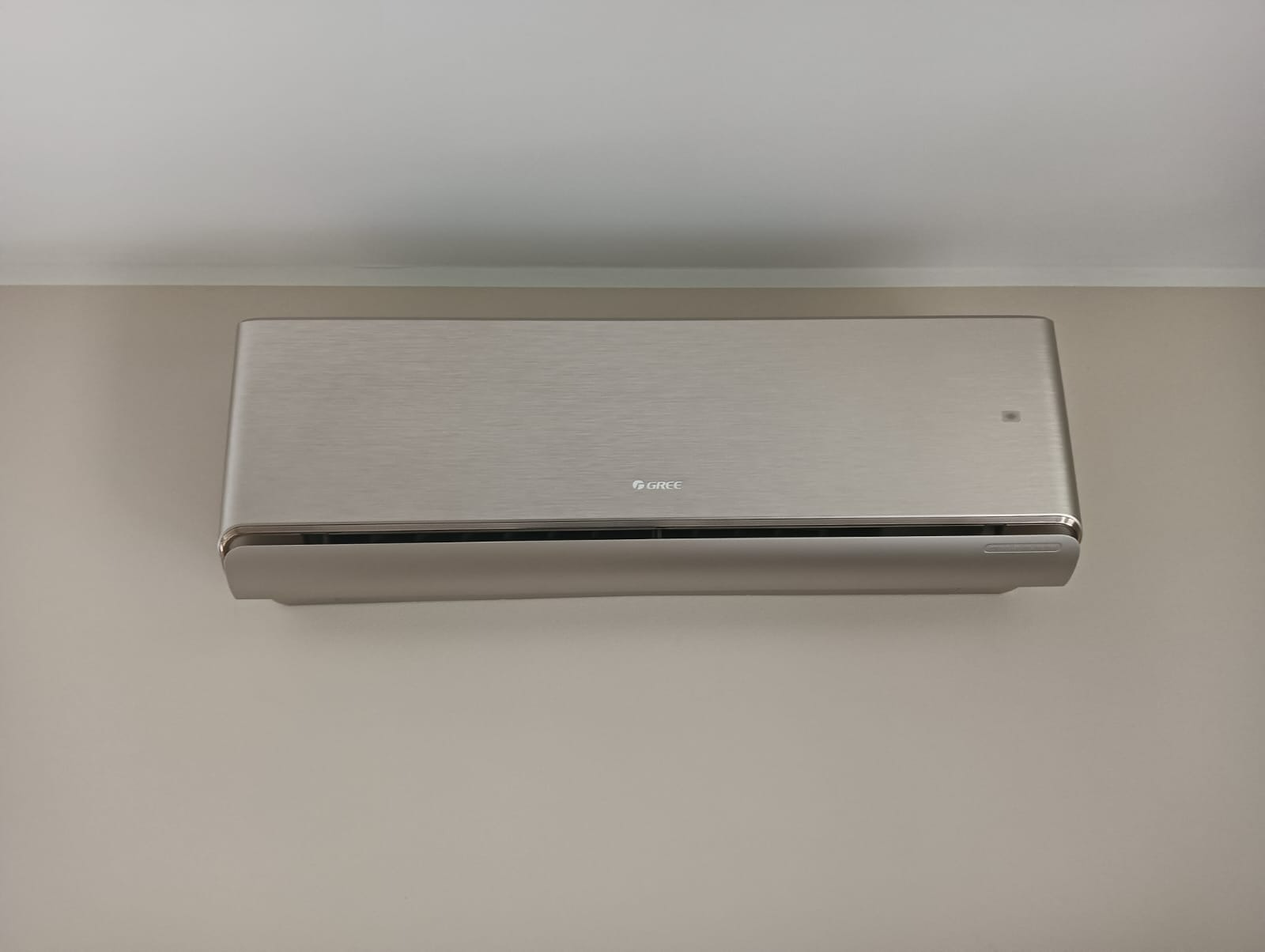 Elegancki, srebrny klimatyzator marki Gree zamontowany na jasnej ścianie w pomieszczeniu.