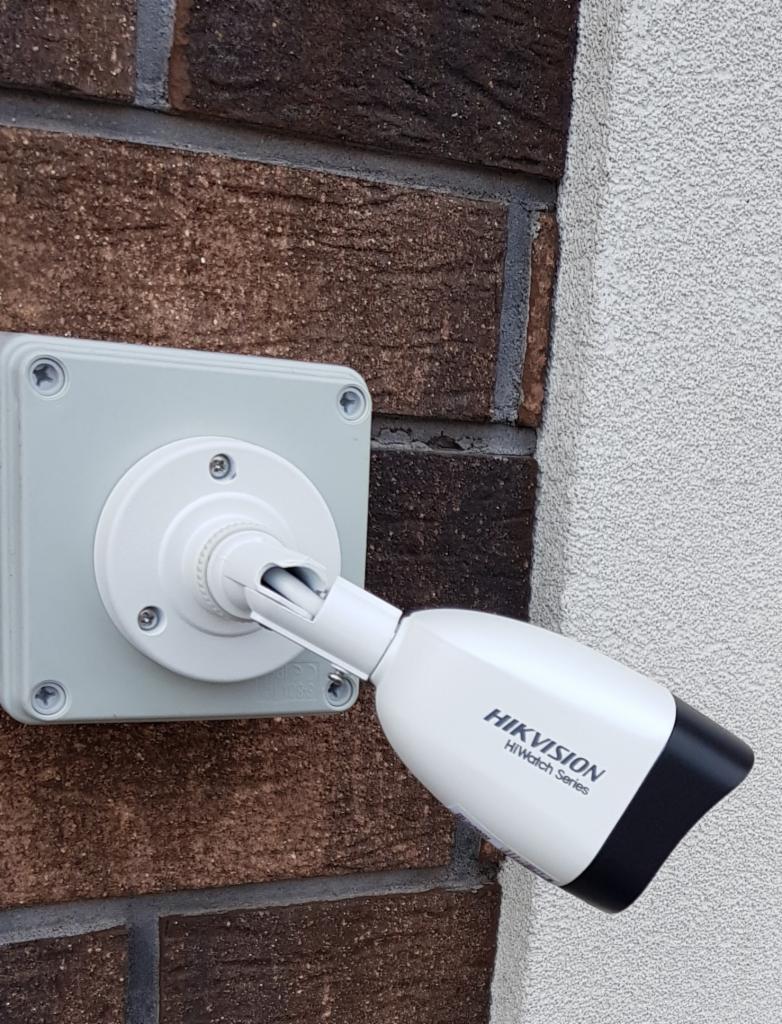 Zewnętrzna kamera monitoringu Hikvision HiWatch Series zamontowana na ceglanej ścianie, widok z boku.