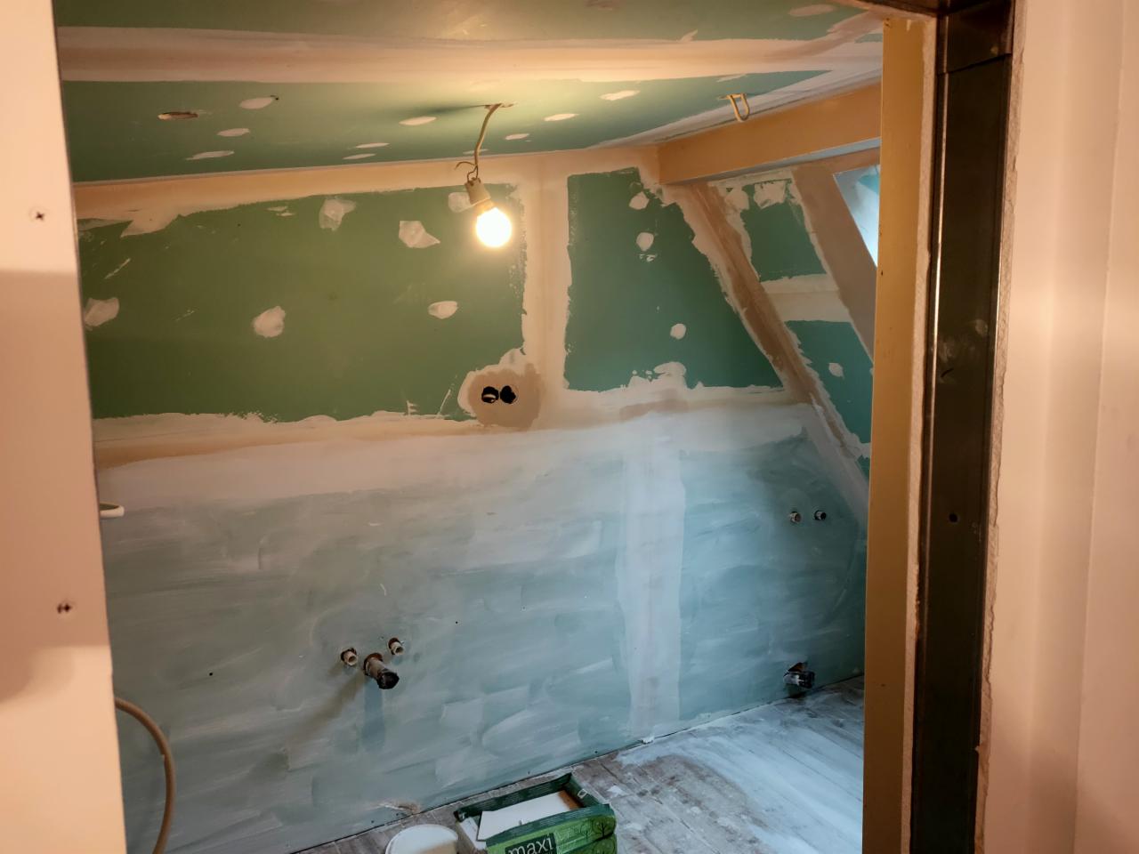 Poddasze w trakcie remontu: ściany i skośny sufit pokryte zielonymi płytami gipsowo-kartonowymi, widoczne łączenia szpachlowane, instalacja elektryczna i hydrauliczna wyprowadzona, surowe drewniane...