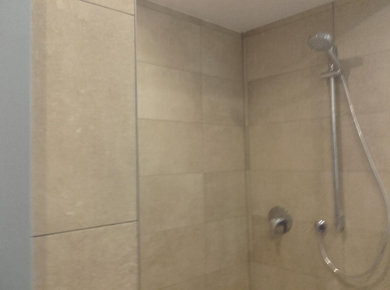 Beżowe płytki w kabinie prysznicowej z zamontowaną baterią i słuchawką prysznicową.