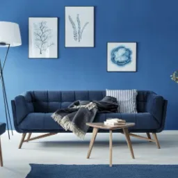 Niebieski salon z sofą, lampą podłogową, stolikiem kawowym i dekoracjami ściennymi w tonacji niebieskiej.
