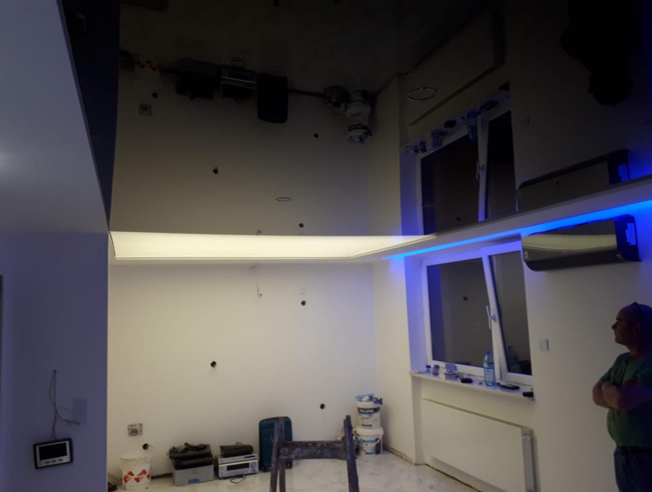 Wnętrze w trakcie remontu z podwieszonym sufitem z oświetleniem LED, widoczne przygotowania do malowania ścian i instalacji klimatyzacji, na podłodze drabina i narzędzia.