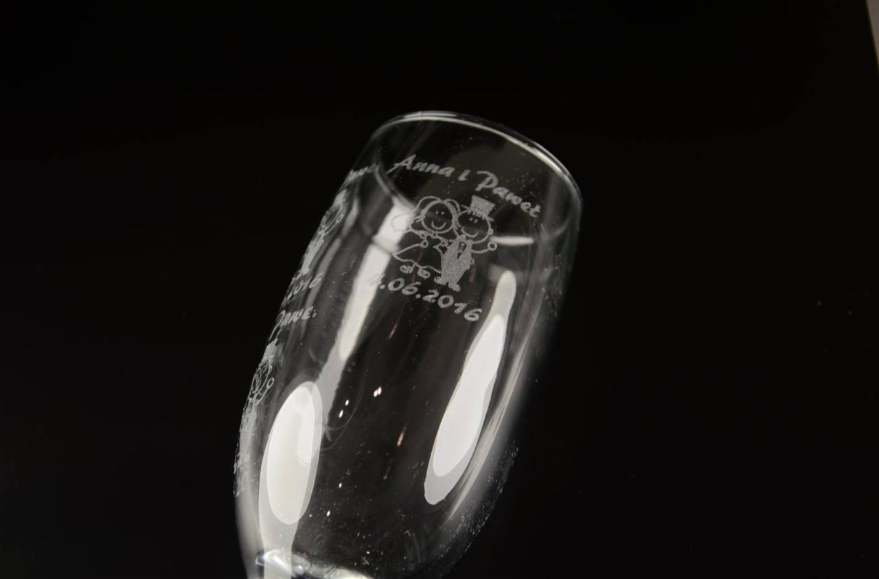 Kieliszek do szampana z wygrawerowanymi imionami Anna i Paweł, datą ślubu 4.06.2016 oraz rysunkiem pary młodej, na czarnym tle.