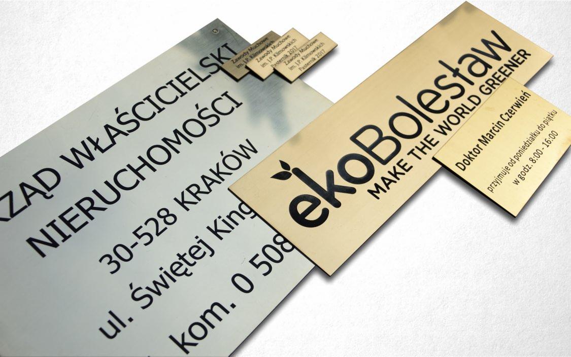 Zestaw metalowych tabliczek informacyjnych i szyldów firmowych w kolorze srebrnym i złotym, z czarnym drukiem, prezentujących nazwy firm, adresy i godziny przyjęć.