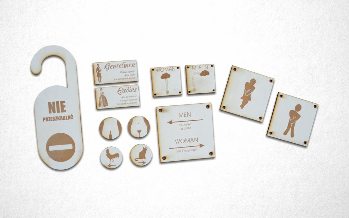 Zestaw drewnianych tabliczek informacyjnych i zawieszki na klamkę z napisami i piktogramami, przedstawiających oznaczenia toalet, prośbę o nie przeszkadzanie oraz humorystyczne napisy.