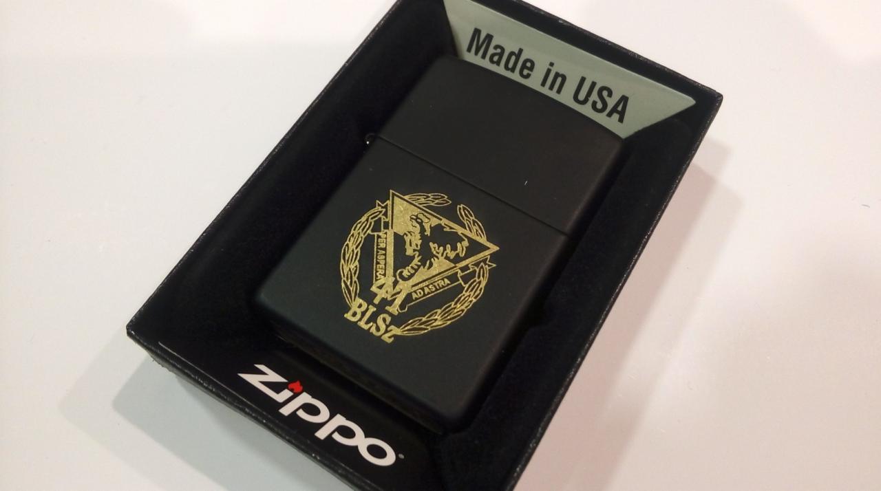 Czarna zapalniczka Zippo z grawerowanym złotym orłem i napisem 'Per Aspera Ad Astra' w pudełku z napisem 'Made in USA'.