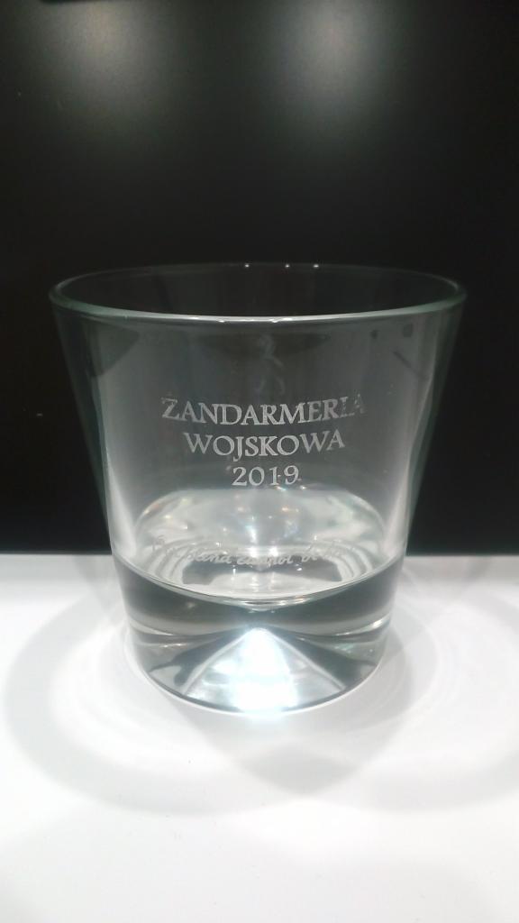 Szklanka z wygrawerowanym napisem 'Żandarmeria Wojskowa 2019' na czarnym tle.