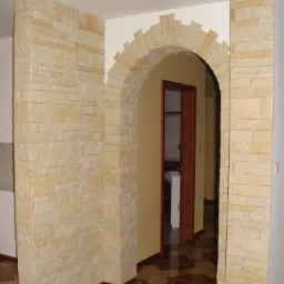 Kamienna kolumna i łukowe przejście wykończone piaskowcem wewnątrz domu, widok na łazienkę z brązową futryną drzwi i wzorzystą podłogą.